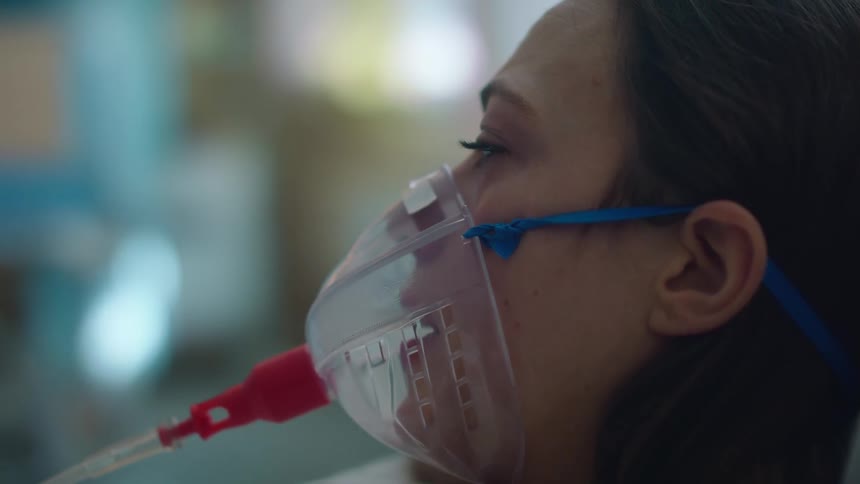 Young woman laying in bed with an oxygen mask on a hospital
