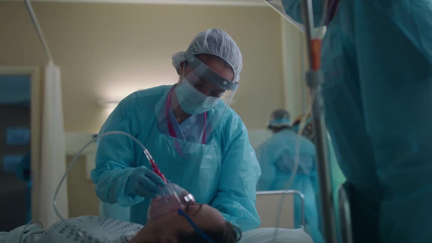 Medical personnel in protective gear work over patient