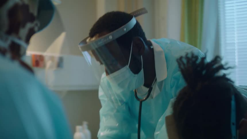 Doctors and nurses wearing protective clothes and face masks helping a patinent in a hospital room