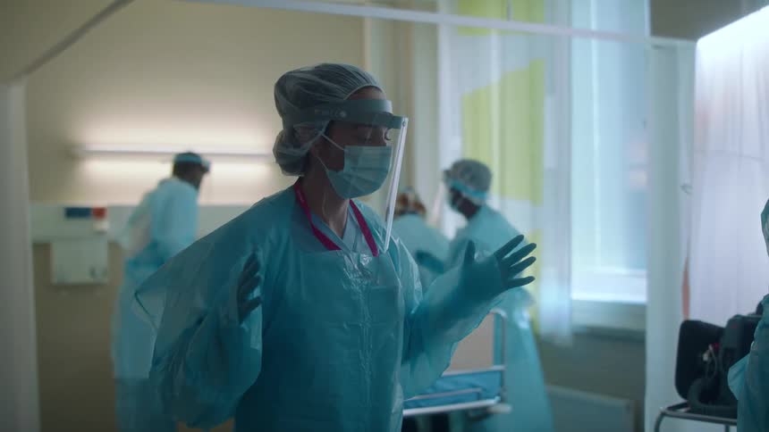 Young doctor wearing protective gear waits for instructions near a hospital bed
