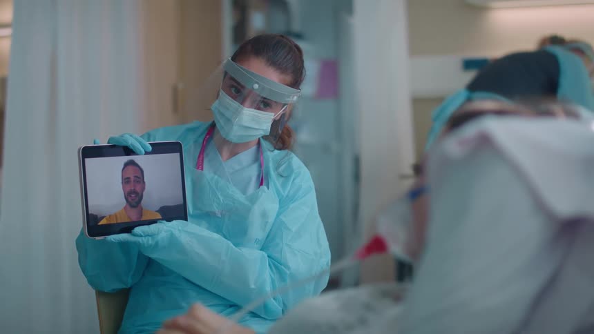A nurse holds a tablet up so a female patient can speak to a man during a video call