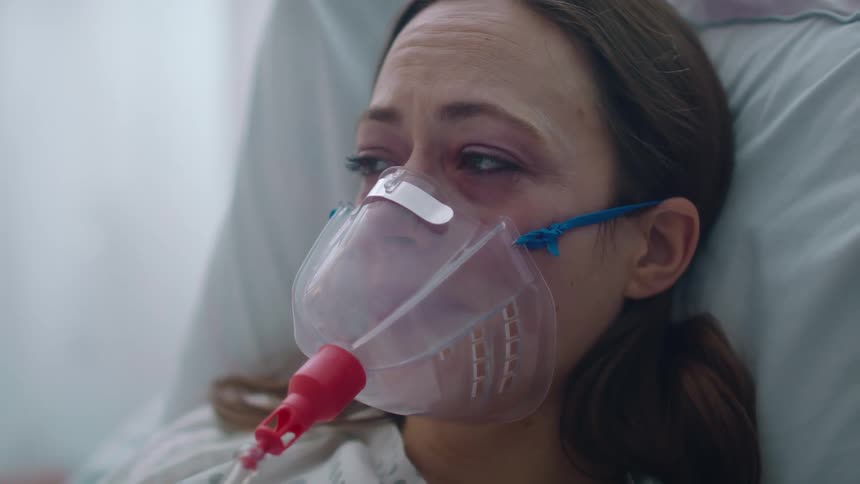 A woman is lying in a bed with an oxygen mask on her face