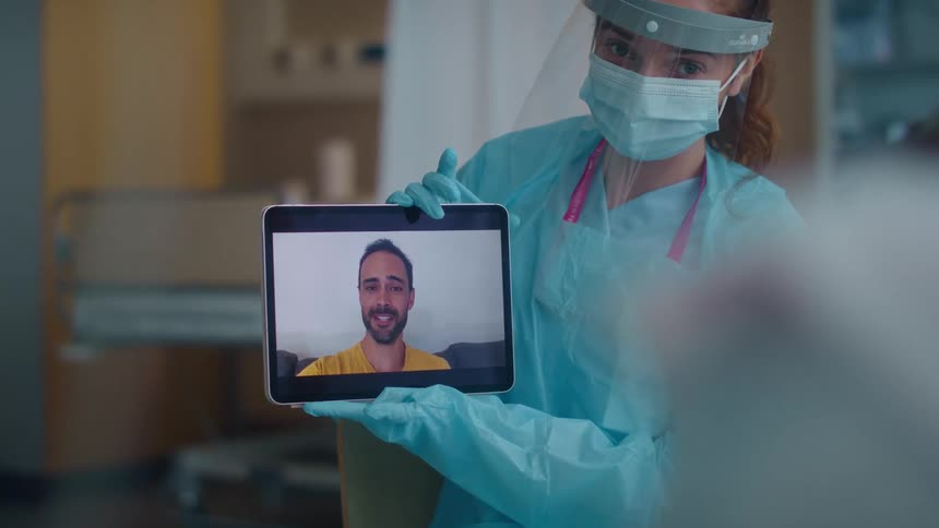 A doctor holds a tablet up to a patient to talk to a person