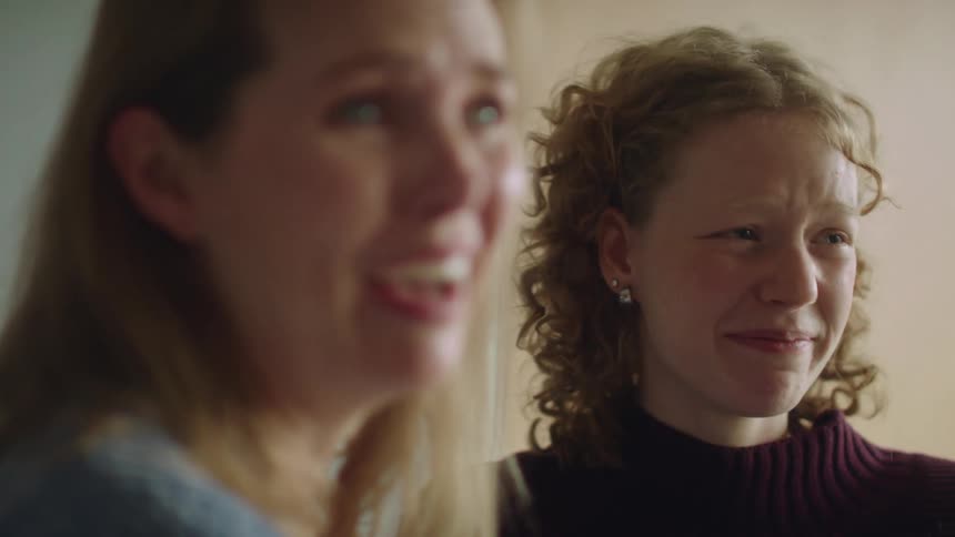 Two women in a room smiling with a wall in the background