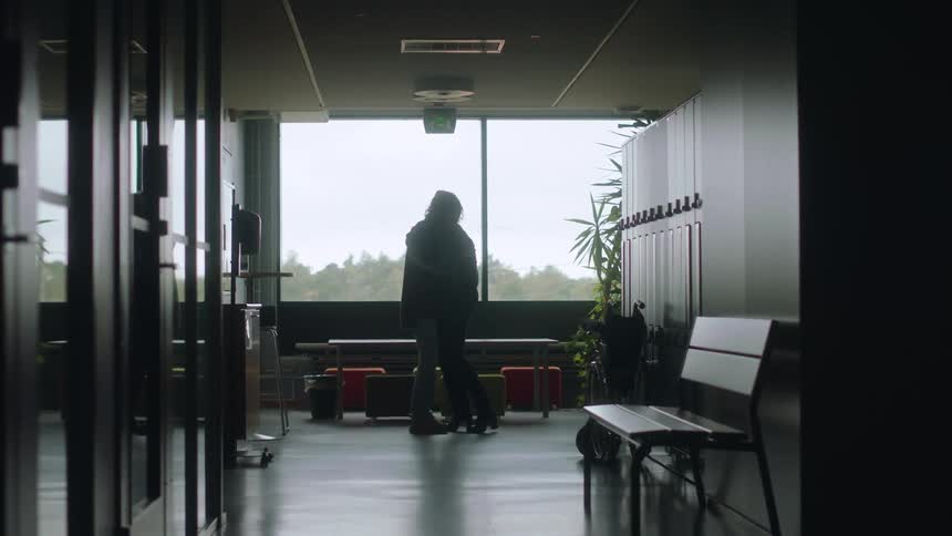 Middle aged woman cuddling sad woman are silhouetted against the cloudy sky in hospital corridor
