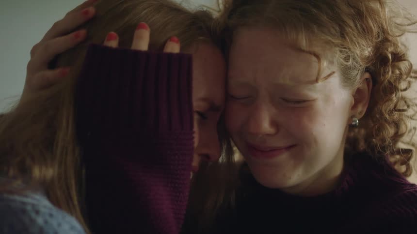 Two women in a room smiling and crying with a wall in the background