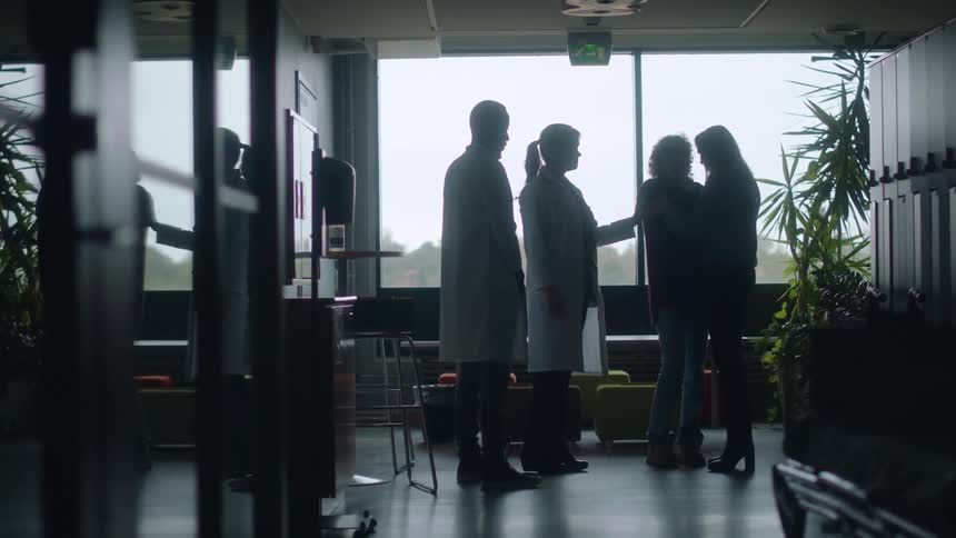 Medical staff console sad woman crying and cuddling middle aged woman in hospital corridor