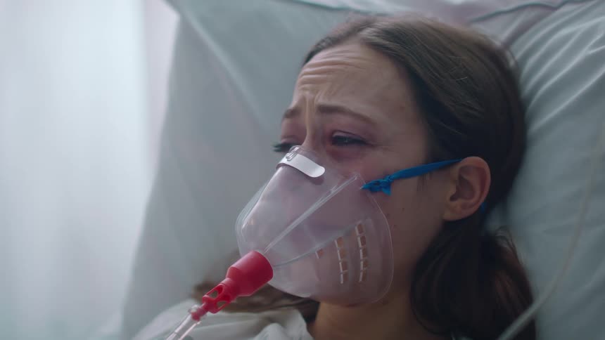 A worried woman rests in a hospital bed while wearing a cpap mask
