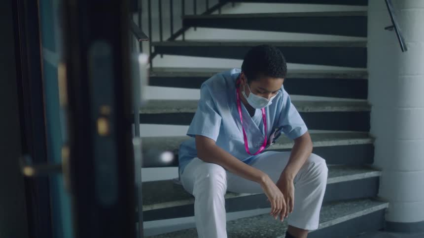 A nurse sits with her bowed down in a stairwell