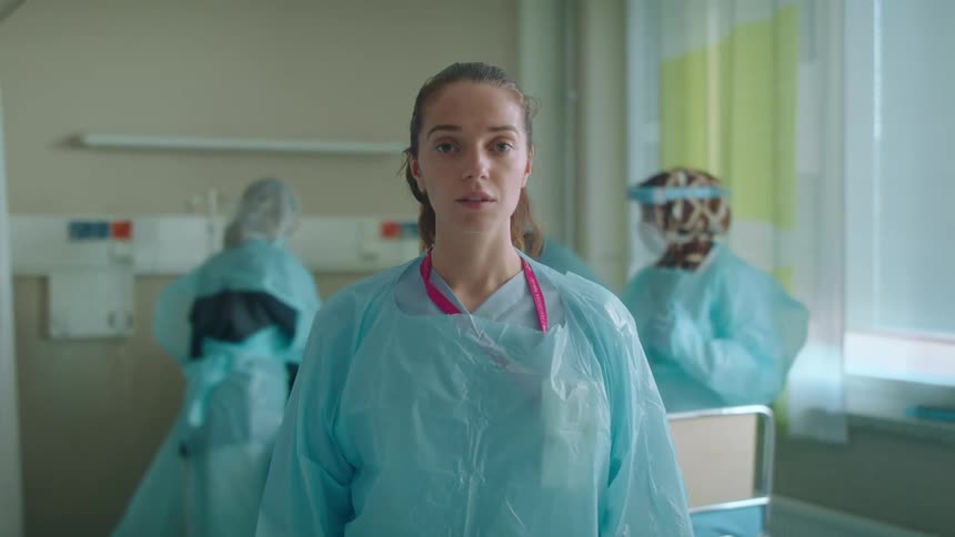 A woman stands still as other doctors work