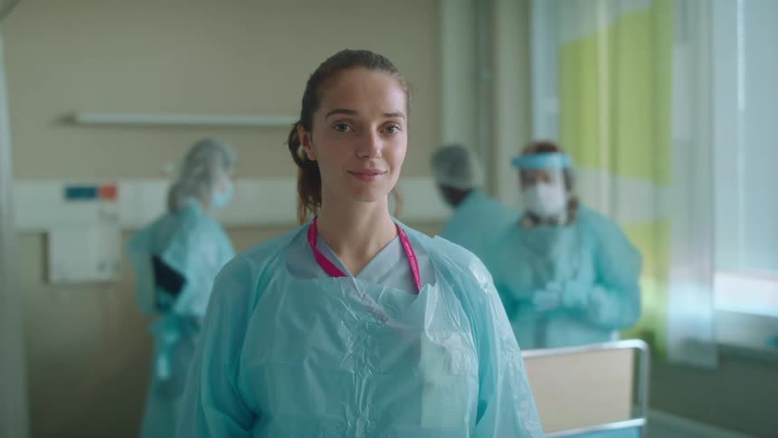 A nurse in the hospital staring with doctors nurses a wall and window in the background