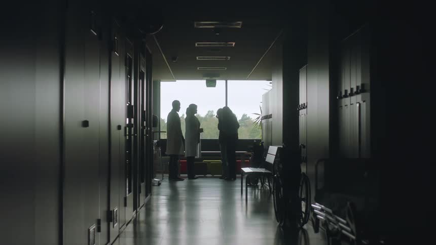 Two doctors at the end of a hospital hallway talking to two women