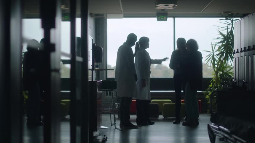 Female and male medical doctors inform and console patient standing in hospital corridor