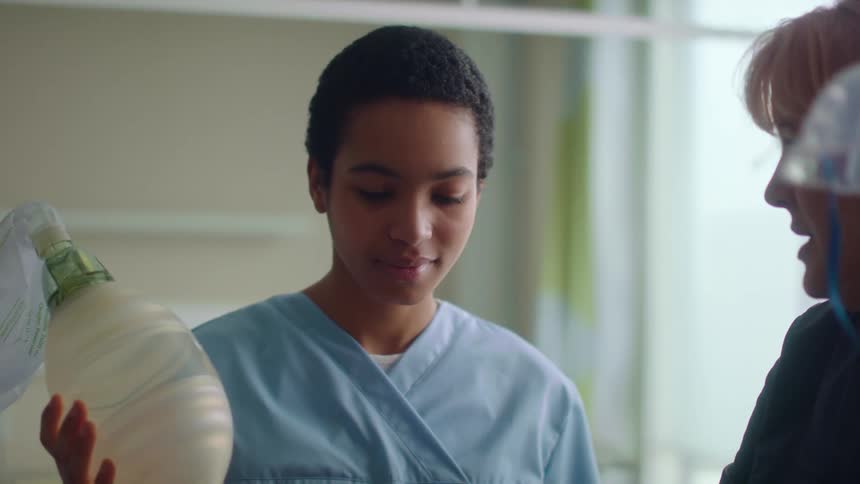 A nurse nods along while listening to another nurse in a patients room