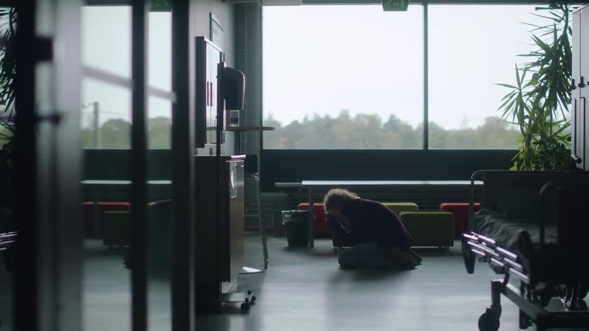 A woman is standing in a hospital and she falls to her knees crying
