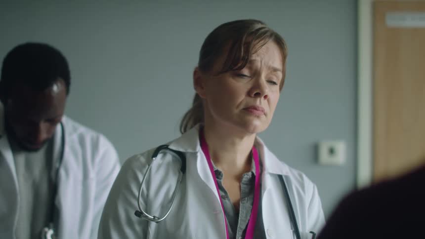 Two doctors in a room looking worried are speaking to a person