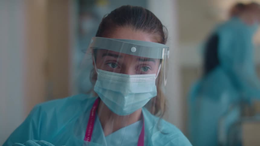Sad nurse with mask and scrubs holds tablet to show the patient video call