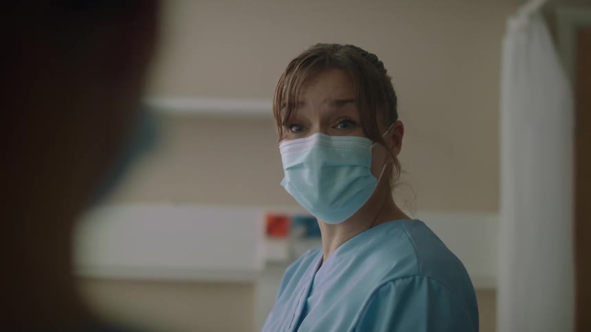 Nurse wearing face mask talks and smiles in hospital room