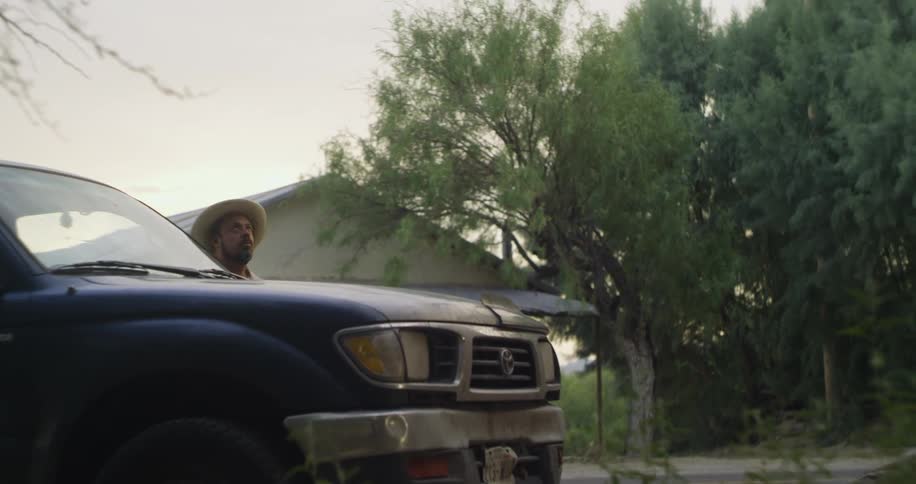 A man wearing a sombrero gets out of a truck and goes inside a building