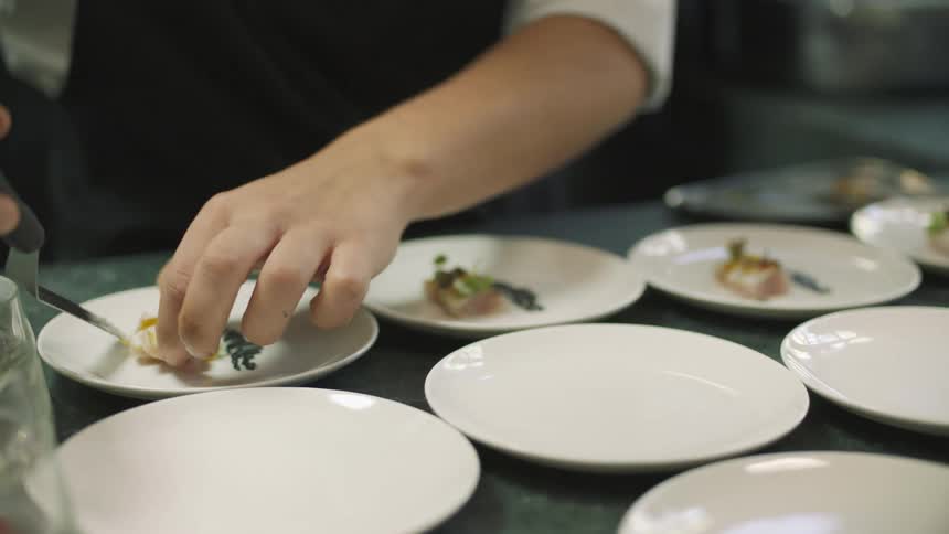 A chef is plating food onto dishes on a counter top in a kitchen