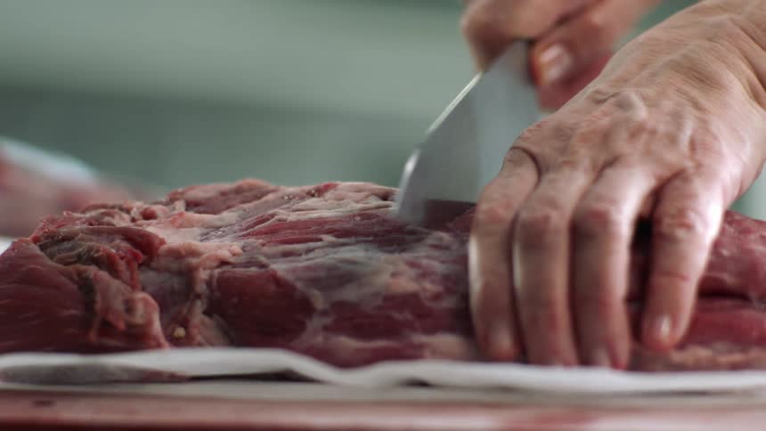 A person using their hands to chop and slice meat on a counter top