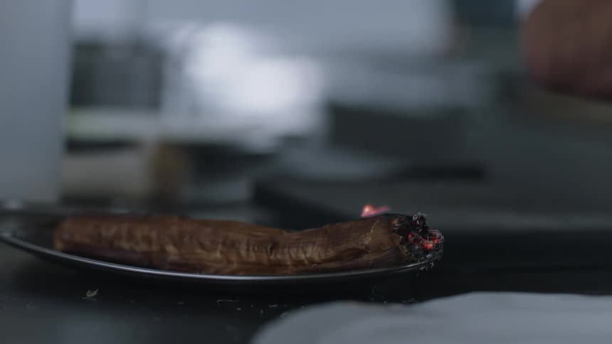 Flames from a torch sear and burn the end of food on a small platter