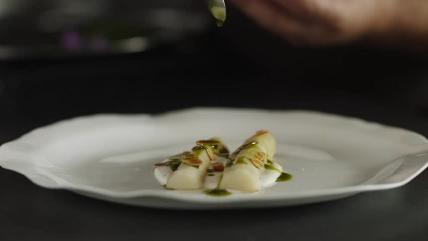 Chef dressing and garnishing a dish over a white porcelain plate