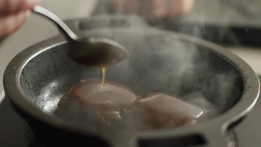 A person spoons freshly made caramel on top of brownies in a pan