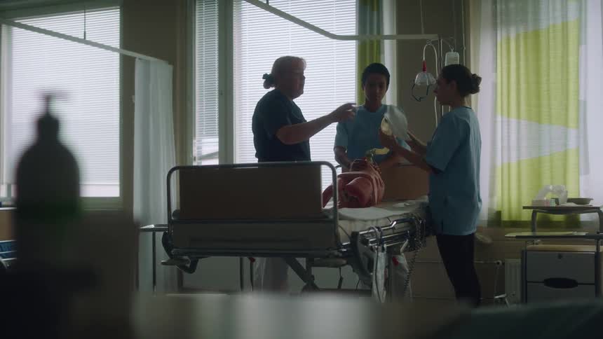 A nurse gestures and explains as she trains two students on bagging a patient using a dummy