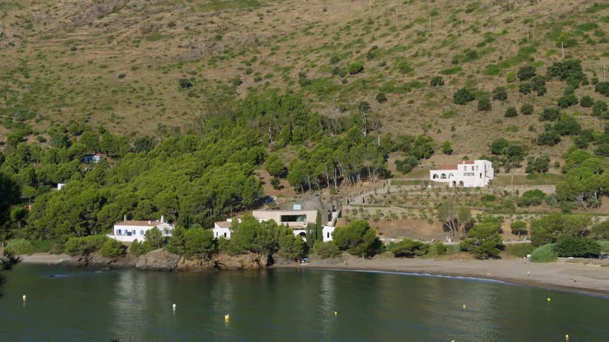 White homes at the base of a hill near a sandy beach and serene lake