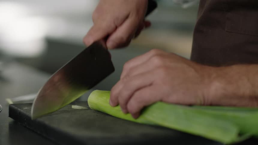 Someone is holding a knife and slicing a leek