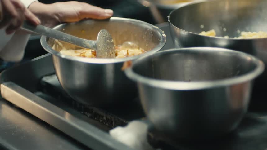 Chef adds cooked bacon to mixture in pot stirring it in as flame burns under stove top burner