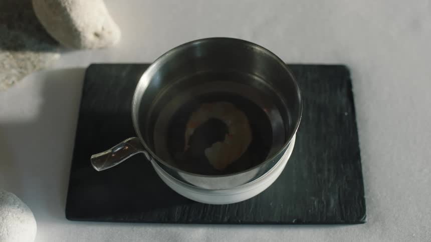 A person lifts the lid off a pot cooking a single shrimp