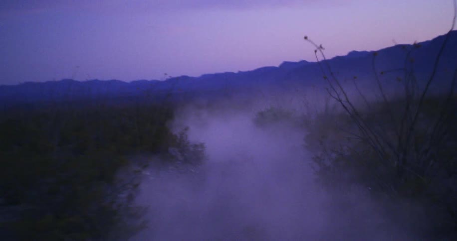 Dust kicking up on a dirt road on the field near the mountains at evening