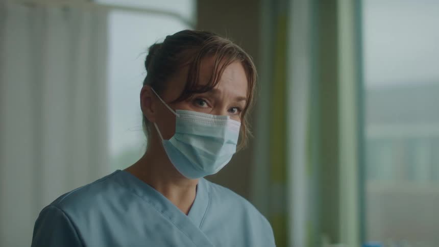 A doctor in scrubs talking to someone in a hospital room