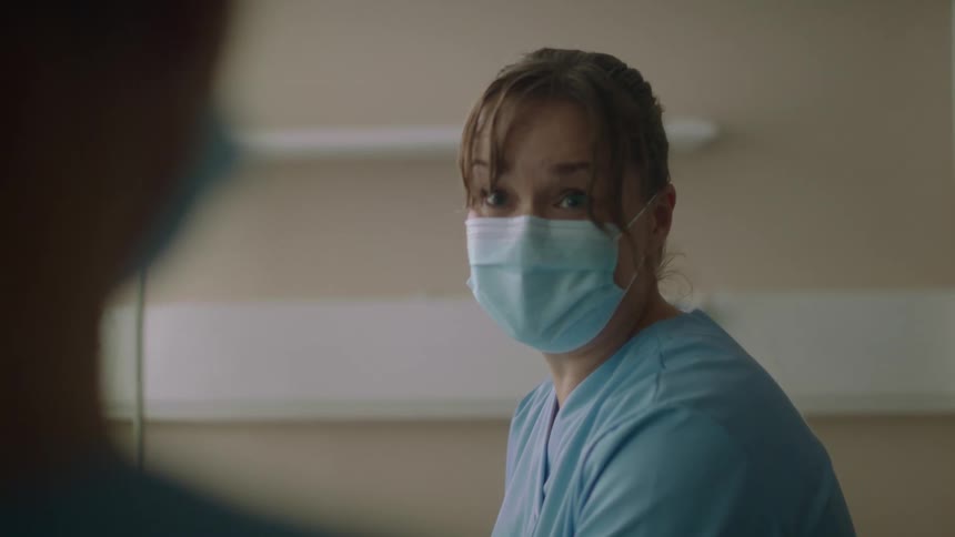 Doctor wearing a blue disposable face mask teaching a nurse how to perform a procedure