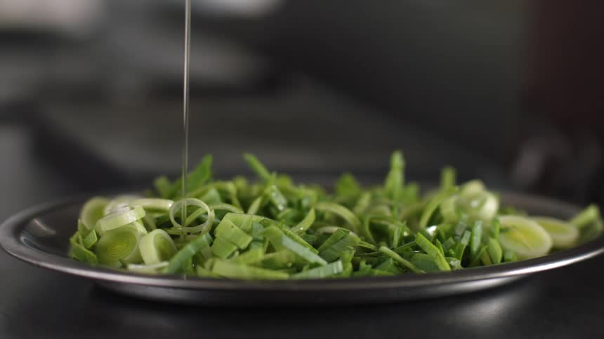 Clear sauce is drizzled onto plate of sliced green onions