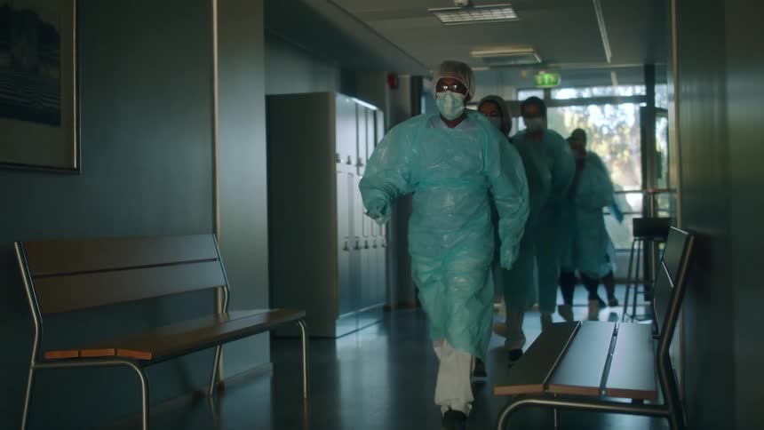 Medical team dressed in scrubs and protective gear walks along hallway in hospital