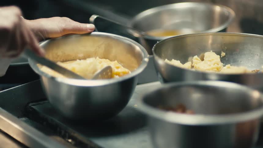 Chef with white shirt puts a spoonful of mashed potatoes in the pot in the kitchen