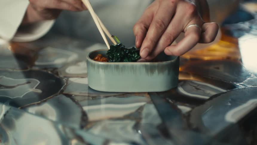 Cook with white shirt puts food in small bowl with chopsticks in restaurant