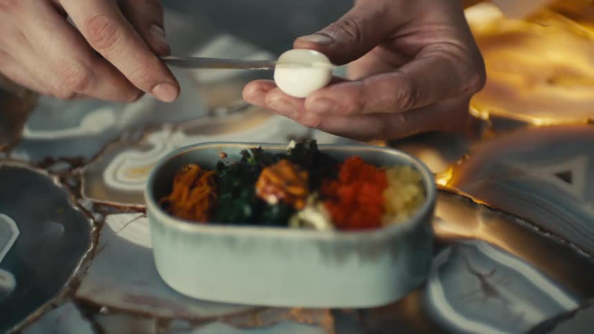 Someone is slicing a hard boiled egg over a dish of food
