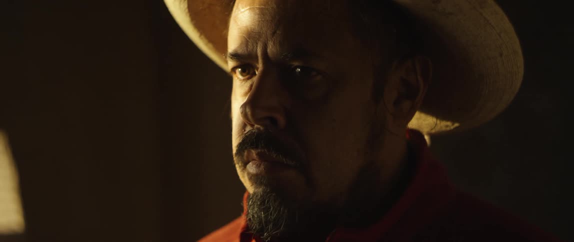 Man with hat beard and red shirt stares into space