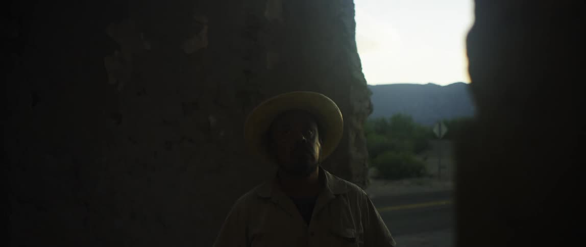 Hispanic man wearing a hat looking around inside the mouth of a cave