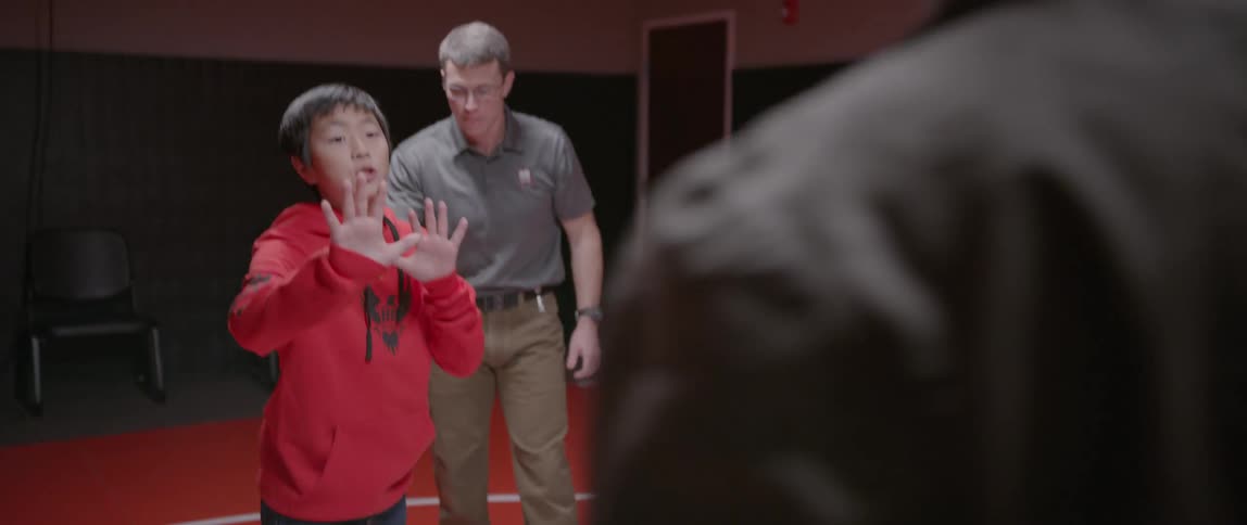 A young boy with a coach standing behind him reacts to an attacker in a self-defense class