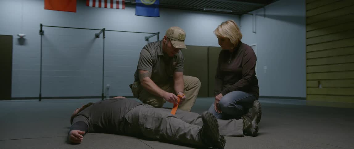 A man shows how to tighten a strap on another person's leg