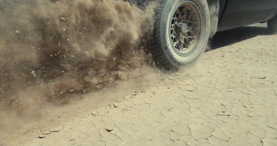 A vehicles rear tire kicks up dirt and dust as it drives through the desert
