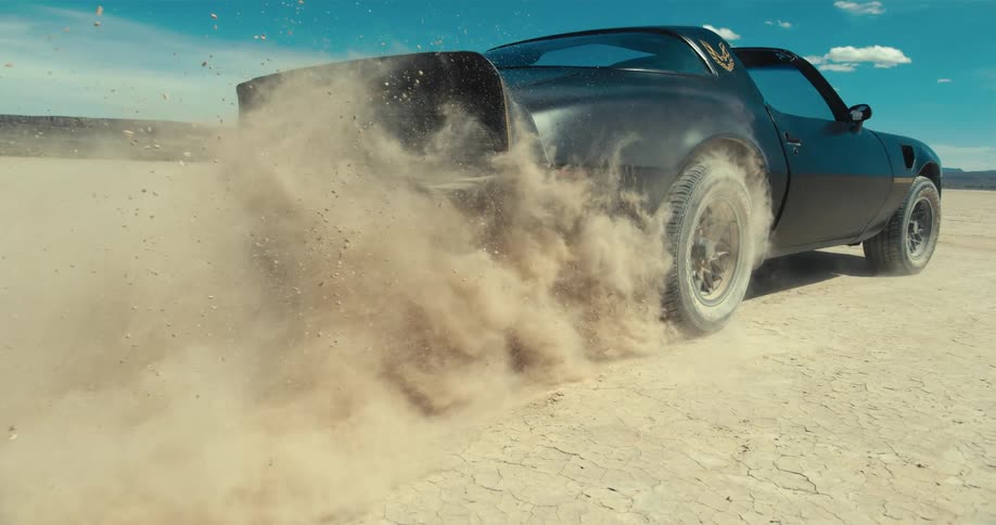 A car driving on a desert with a mountain range the sky and clouds in the background