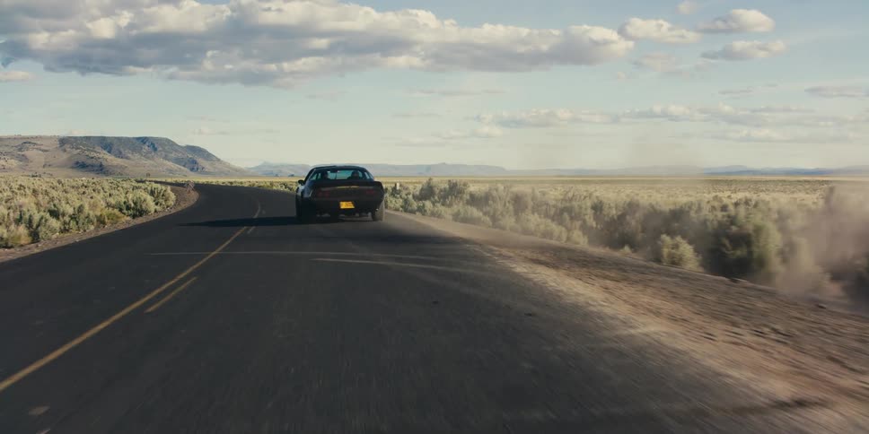 A car driving on a road on a desert landscape with the sky and clouds in the background