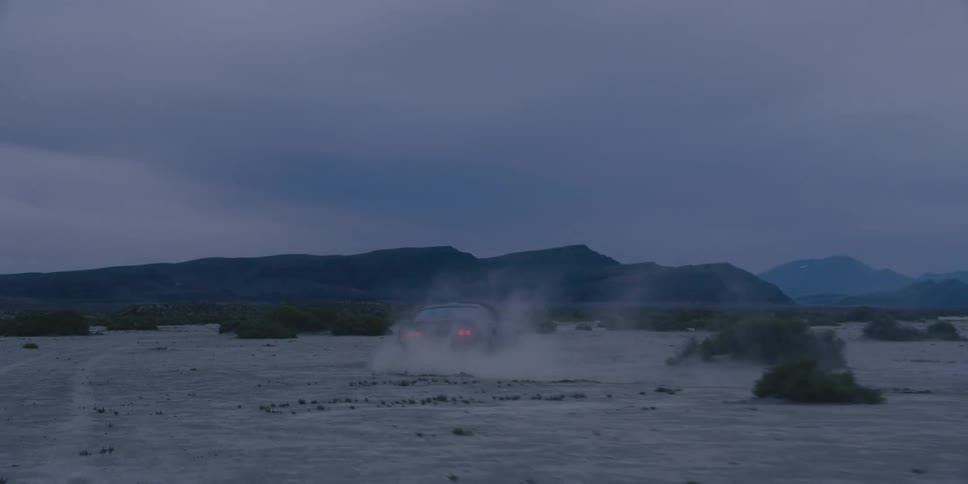 A car driving around in the desert at dusk