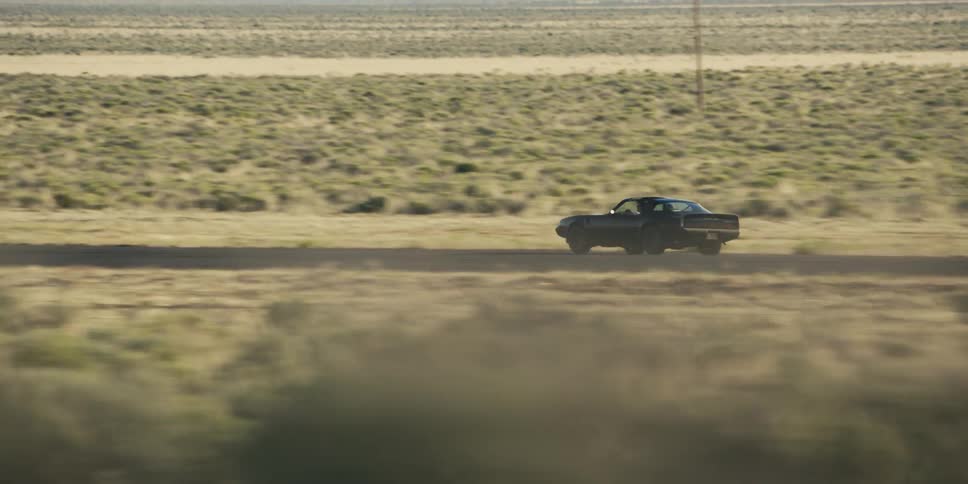 A sports car travels on an empty desert road on a hazy sunny day